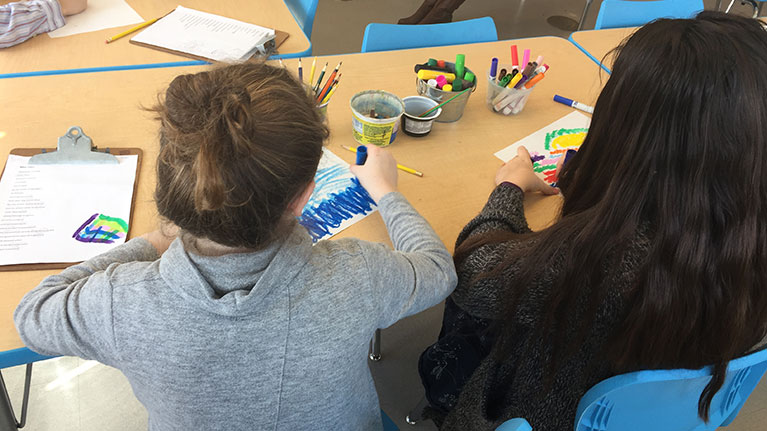 The back of two girls coloring at a desk