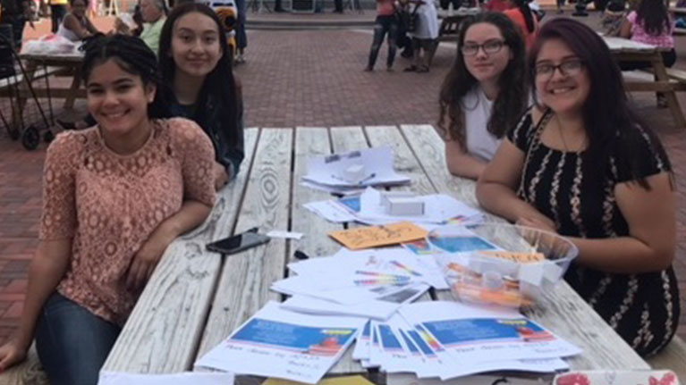 Group of four girls sitting at a picnic table together with flyers